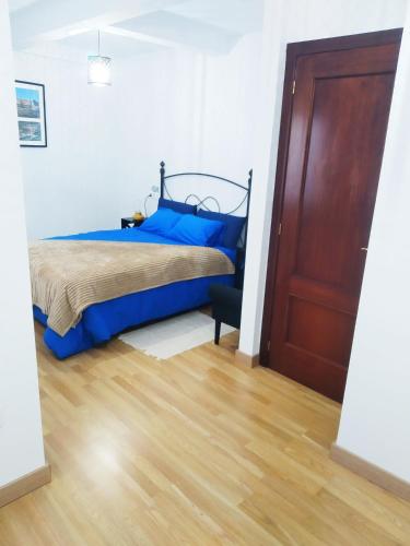 a bedroom with a bed with blue sheets and a wooden floor at LA CASINA DE HUGO AZUL centro Luanco in Luanco