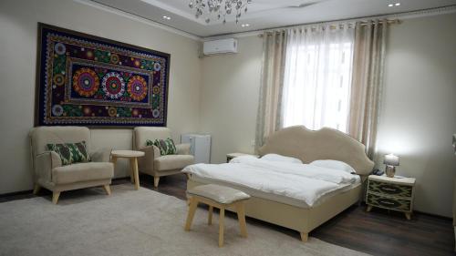 a bedroom with a bed and two chairs and a painting at Hepci Hotel Istaravshan in Ŭroteppa