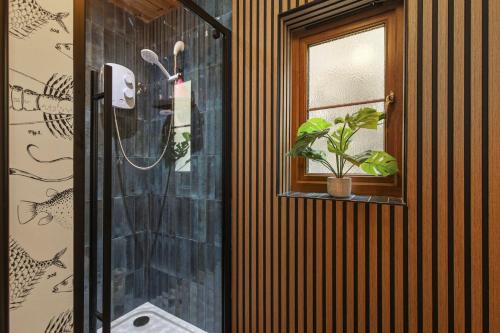 a bathroom with a shower with a window and a plant at Bay View - holiday cottage by the sea with stunning views in Pendine