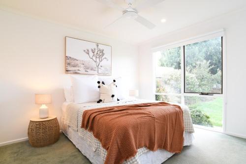 a white bedroom with a bed and a large window at The Salt Shack in Mallacoota