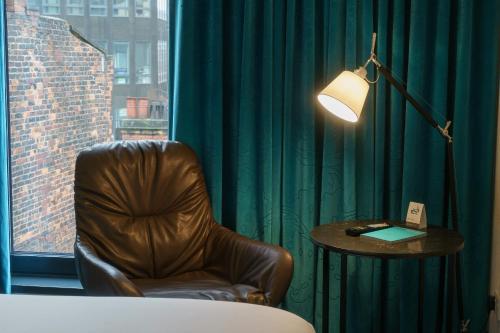 a room with a chair and a table and a lamp at Motel One Koblenz in Koblenz