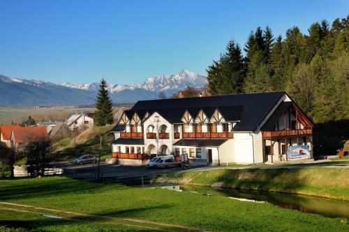 a large white building with a black roof next to a river at Penzión ZIVKA in Závažná Poruba