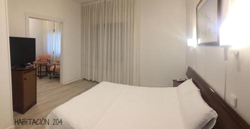 a bedroom with a white bed and a television at Hostal Vista Alegre in Castro-Urdiales