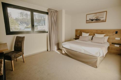 a bedroom with a bed and a chair and a window at Le Nautica Hôtel in Perros-Guirec