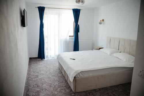 a bedroom with a bed with blue curtains and a window at Armonia -Rucar in Podu Dîmboviţei
