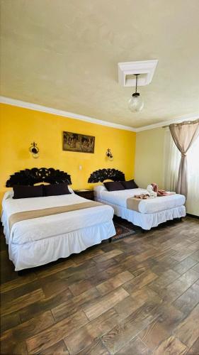 two beds in a room with yellow walls at La Chacra de Joel Hotel in Huehuetenango