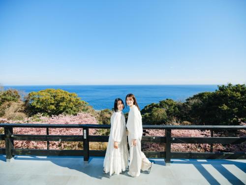 two women in white robes standing on a balcony with the ocean at UMI SORA VILLA 伊豆河津 in Kawazu