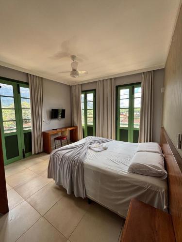 a bedroom with a bed and a desk and windows at Pousada Solar dos Guarás in Catas Altas