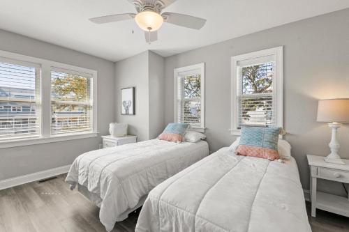 two beds in a bedroom with two windows at Just Peachy VillageOBX in Kill Devil Hills