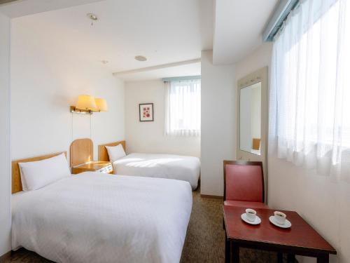 a hotel room with two beds and a table at Hotel Meijiya in Hamamatsu