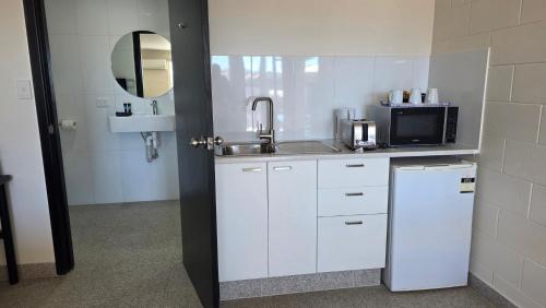 a kitchen with white cabinets and a sink and a mirror at Longreach Most Central Motel in Longreach