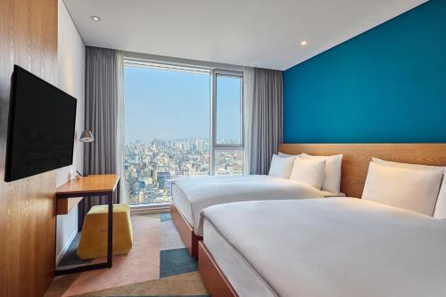a hotel room with two beds and a large window at L7 HONGDAE by LOTTE HOTELS in Seoul