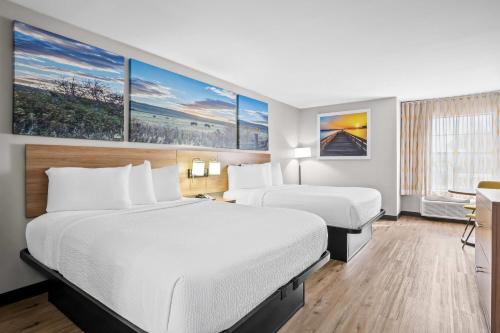 a hotel room with two beds and paintings on the wall at Days Inn by Wyndham Dallas Plano in Plano