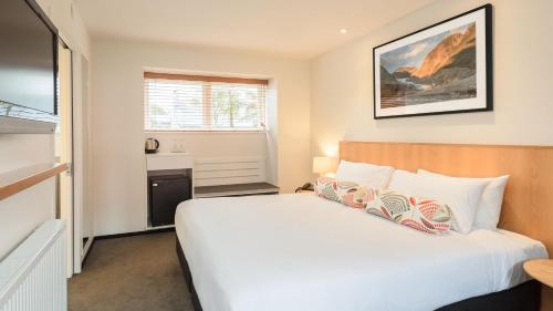 a bedroom with a white bed and a window at Heartland Hotel Glacier Country in Fox Glacier