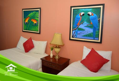 two beds in a room with paintings on the wall at Hotel y Apartments Los Cisneros in Managua