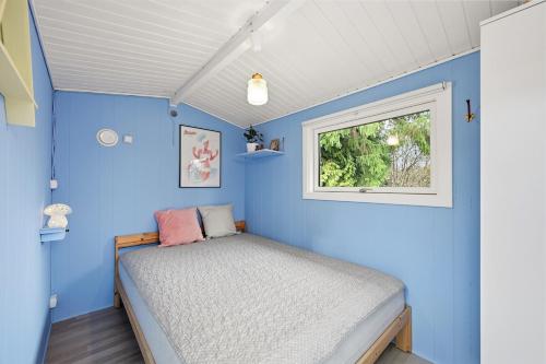 a blue bedroom with a bed and a window at Sommerhusidyl med vildmarksbad, strand og udebruser in Jægerspris
