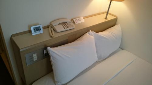 Hotel Crown Hills Sagamihara في ساغاميهارا: سرير مع هاتف ومخدة في الغرفة