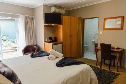 a hotel room with a bed and a desk and a television at Kududu Guest House in Addo