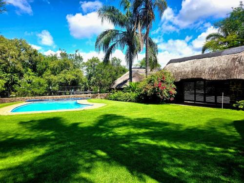 a shady yard with a thatched building and a swimming pool at Lapa Phanzi Game Lodge in Modimolle