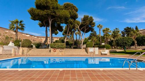 a swimming pool with palm trees and a building at EVH114 Casa con piscina comunitaria in Altafulla