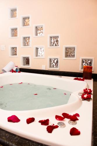 a bathtub filled with water with red roses on the floor at Hotel Dom Otto in Vespasiano