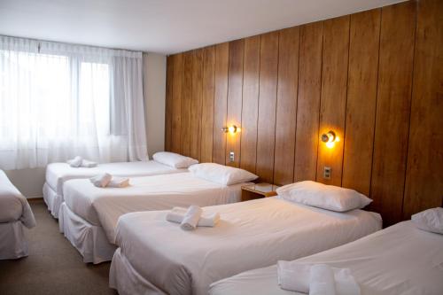 a hotel room with four beds with white sheets at Hotel Germania in Puerto Varas