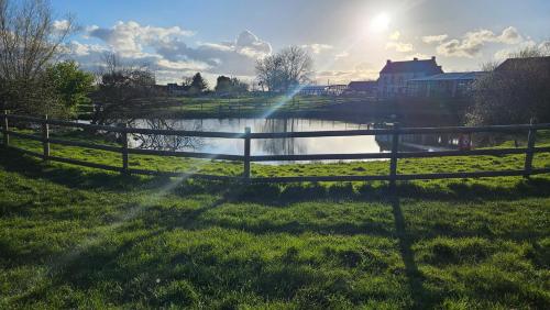 a fence next to a river with the sun shining at Mobilhome Normandie in Litteau