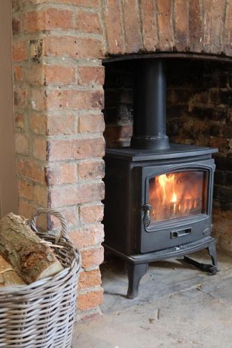a stove in a brick fireplace next to a basket at Plum Cottage in Cottesmore