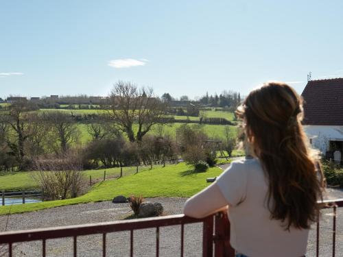 a woman standing on a fence looking out at a field at Écodomaine le Vérin, Gîtes et spa - Mer, Nature & Confort - Côte d'Opale in Wierre-Effroy