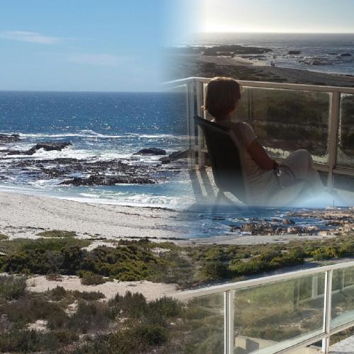 a woman sitting in a chair on a balcony looking at the ocean at Seester Accommodation in Lambertʼs Bay