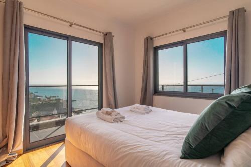 a bedroom with large windows and a bed with towels on it at Camara De Lobos Lux Villa in Câmara de Lobos