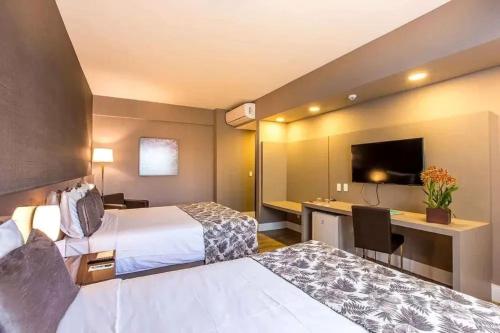 a hotel room with two beds and a desk at Tauá Hotel & Convention Atibaia in Bairro Rio Abaixo