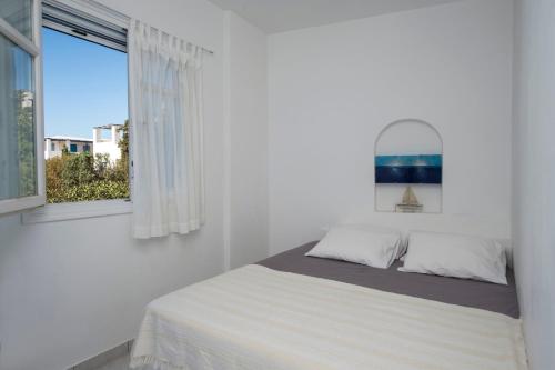 a white bedroom with a bed and a window at Aiolos Home with private veranda and amazing sea views, Paros in Piso Livadi