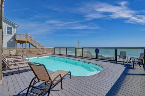 a swimming pool on a deck with chairs and the ocean at Tipsy Turtle North- Oceanfront Oasis - Pool - Dog Friendly in Surf City