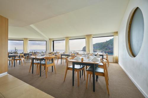 a dining room with tables and chairs and windows at Caloura Hotel Resort in Caloura
