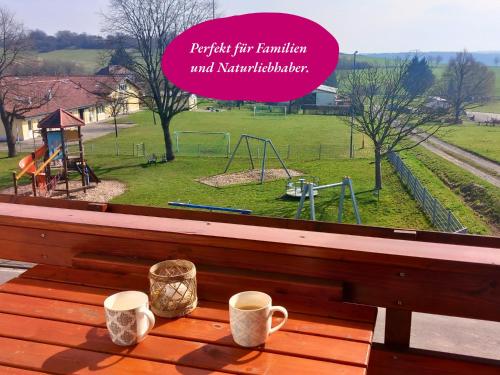 a table with two cups of coffee on a bench with a playground at Ferienwohnung Matheaperle mit Infrarotkabine in Nidda