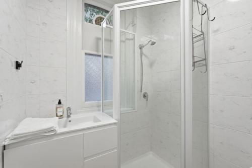 a white bathroom with a shower and a sink at Charming Sandy Bay Cottage in Sandy Bay