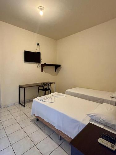 a room with two beds and a tv on the wall at Bravo Inn Hotel Coxim in Coxim