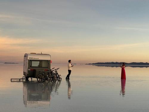 a man and a woman standing in the water next to a trailer at Camper Elegance Uyuni - All Inclusive in Carpas