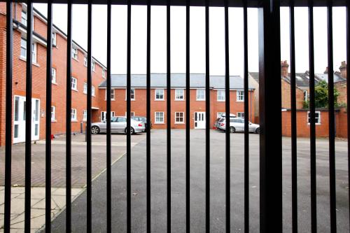 a fence with cars parked in front of a brick building at Leamington Spa Apartments in Leamington Spa