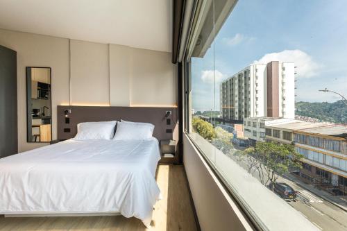a bedroom with a white bed and a large window at Break Estudios Manizales in Manizales
