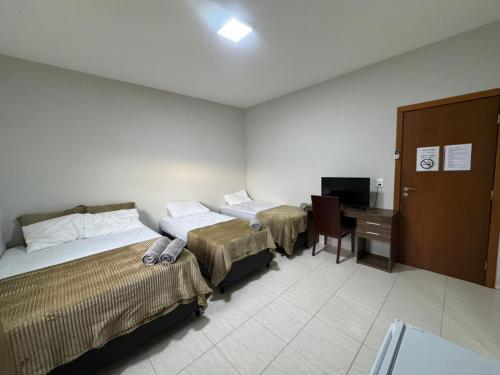 a room with two beds and a desk and a television at Alvorada Hospedagem in Jataí