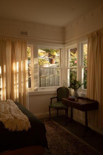a bedroom with a bed and a desk and windows at Whimsy Cottage, Beachside retreat, Outdoor bath in Kingston Beach