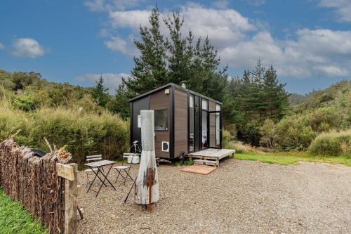 a black tiny house with a bench and a fence at Te Paki Dam View X by Tiny Away in Sanson