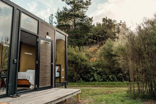a small house with a large window and a wooden bench at Te Paki Dam View X by Tiny Away in Sanson