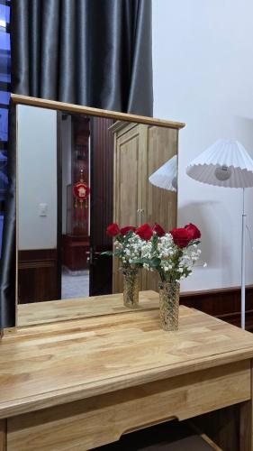 two vases with flowers on a table with a mirror at Rose House - Quảng Bình in Bố Trạch