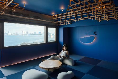 a woman sitting in a room with a table and a window at Art House HINODE 10 people 3 minutes from the station Art and Tokyo Bay spectacular ocean view in Tokyo