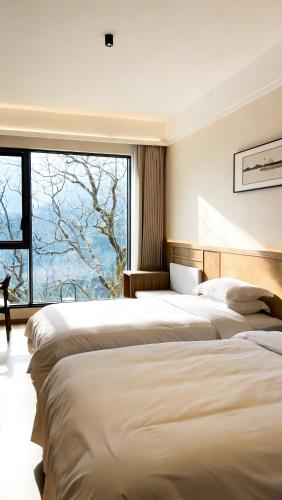 two beds in a room with a large window at 重庆金佛山古核隐庐Resort Hotel in Nanchuan