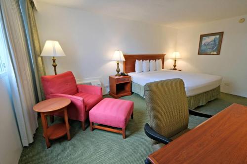 a hotel room with a bed and chairs and a table at Ramada Plaza by Wyndham Waikiki in Honolulu
