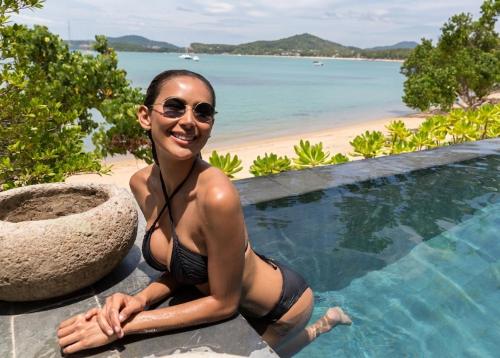 a woman in a bikini sitting next to a swimming pool at Clay Beach Samui - Beachfront Villas in Bophut
